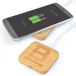 A bamboo wireless charger with a smartphone on top, showing a charging battery icon and featuring a logo.