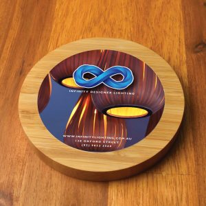 A round bamboo wireless charger with a colorful design featuring a logo, placed on a wooden surface.