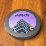 A round, metallic wireless charger with a colorful graphic featuring a modern apartment building.