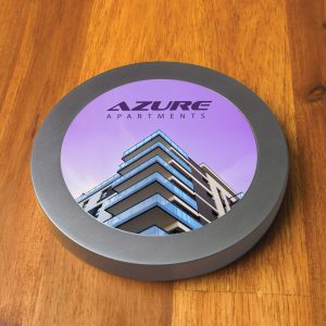 A round, metallic wireless charger with a colorful graphic featuring a modern apartment building.