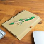 A notebook with a spiral binding and a green Matador pen resting on it, featuring a printed logo.