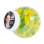 A clear container filled with green and yellow jelly beans, featuring a label with a logo and a portrait.
