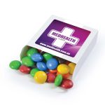 A box filled with colorful chocolate beans, including red, yellow, green, blue, and brown, with a logo on the packaging.