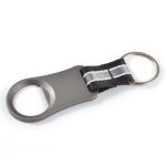 A drink bottle opener featuring a sleek metallic design with a black fabric strap and a keyring attached.