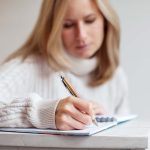 A bamboo pen is being held by a person who is writing in a notebook.