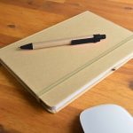 A beige notebook with an elastic band and a brown pen placed on top, resting on a wooden surface.