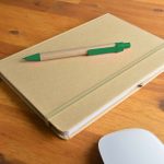 A natural-colored notebook with an elastic band and a green pen resting on top, placed on a wooden surface.