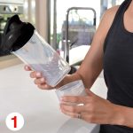 A drink bottle with a black lid and clear body, held alongside a small storage cup.