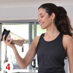 A drink bottle designed for protein shakes, featuring a transparent body and a black lid, held by a woman.