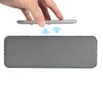 A gray speaker with a textured surface and a hand holding a phone above it, indicating wireless charging.