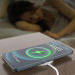 A wireless charger with a sleek design, featuring a green charging icon, placed on a bedside table.