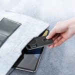 A grey 15W 3-in-1 magnetic wireless charging station being taken from a pocket, with a tablet visible below.