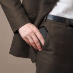 A man in a suit placing a black power bank into his trouser pocket. The power bank has a sleek design and a branding logo.
