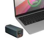 A green power bank with digital display sits next to a laptop, featuring USB ports for charging.