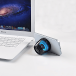 A Bluetooth speaker stand with RGB LED light in black, positioned beside a laptop and a smartphone.