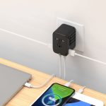 A black travel adaptor plugged into a wall socket, with charging cables connected to a laptop and smartphone on a table.
