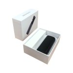 A black charging case for earbuds sits inside a white box, featuring a sleek design and minimalistic packaging.