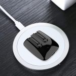 A pair of black magnetic TWS earbuds resting on a round charging pad on a wooden surface.