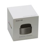 A compact black wireless speaker in a white box featuring a branded logo and model number.