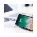 A wireless charger stand with a black finish, holding a smartphone displaying a charging icon, beside a laptop and documents.