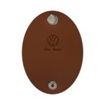 A brown oval-shaped key holder with a metallic button and an embossed logo, featuring the name "Das Auto."