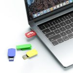 A collection of colourful flash drives—red, green, blue, and yellow—plugged into a laptop's USB port.