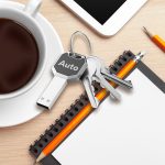 A silver key-shaped USB flash drive rests on a desk beside a coffee cup, notebook, and stationery.