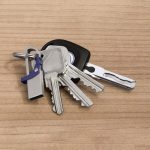 A flash drive in silver and blue, attached to a set of keys, resting on a wooden surface.