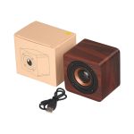 A wooden cube speaker in a rich brown finish, alongside a beige box and a USB cable.