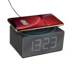 A black alarm clock with a wireless charger on top, displaying the time and a smartphone placed on it.