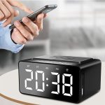 A black alarm clock with a wireless charging area and large digital display, placed on a table.