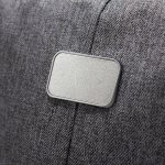 A grey fabric backpack features a textured, rectangular badge on its side, which is likely a logo or branding.