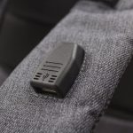 A grey backpack strap featuring a USB port. The fabric has a textured appearance.