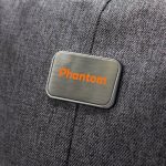 A close-up of a grey fabric with a metallic tag featuring the word "Phantom" in orange. The fabric appears textured.