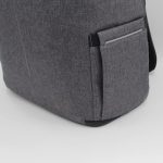 A grey backpack with a side pocket and a logo. The fabric has a textured appearance, adding to its style.