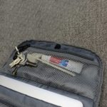 A grey backpack pocket containing keys, a white tube, and a pen, all secured in a mesh compartment.