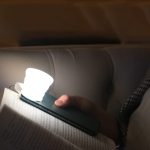 A compact white torch attached to a smartphone, illuminating a book in a dimly lit setting.