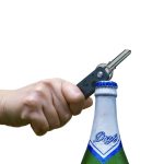 A hand holding a black Keyper Case is opening a bottle with a silver cap. The bottle is green with blue detailing.