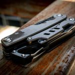 A multi-tool featuring a grey and black design, compact with multiple tools, set on a textured wooden surface.