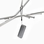 A compact black Bluetooth speaker hanging from a metal frame, featuring a sleek design and a strap.