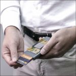 A grey vegan RFID wallet held in hands, displaying several cards inside. The wallet features a subtle logo.