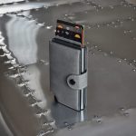 A grey vegan wallet stands upright on a metallic surface, displaying multiple cards partially visible from its opening.