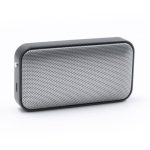 A compact black and silver wireless speaker with a mesh front design and a side port. It features a logo on the surface.