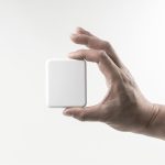 A hand holding a compact, square, white power bank with a sleek design and a soft finish.
