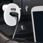 A white Monza car charger with a black USB cable connected, positioned in a vehicle's charging port.