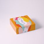 A brightly coloured gift box featuring abstract patterns and a logo on the lid. The box has a yellow background.
