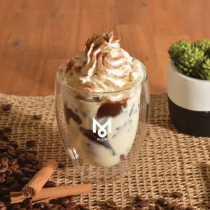 A double wall glass cup filled with a dessert topped with whipped cream, cinnamon, and a logo on the front.