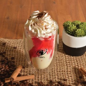 A drink cup featuring a double wall design, clear glass, with whipped cream and a red syrup topping, set on a rustic surface.
