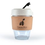 A reusable coffee cup with a clear glass body, a cork band, and a light-colored lid with a straw. It has a logo.