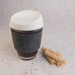 A reusable coffee cup in grey with a white silicone lid and RPET band, accompanied by rolled wafers.
